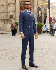 Man in a blue suit standing on a stone pavement with a building in the background